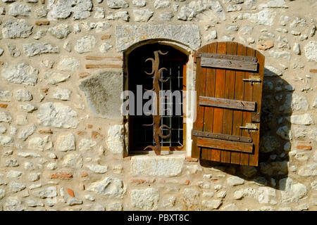 Ein rustikales geschlossenen Fensters mit verzierten Sicherheit Bars in einer Steinmauer in Pujols, Lot-et-Garonne, Frankreich. Dieses historische Dorf ist ein Mitglied der "Les Plus beaux villages de France' Association. Stockfoto