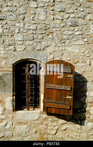 Ein rustikales geschlossenen Fensters mit verzierten Sicherheit Bars in einer Steinmauer in Pujols, Lot-et-Garonne, Frankreich. Dieses historische Dorf ist ein Mitglied der "Les Plus beaux villages de France' Association. Stockfoto