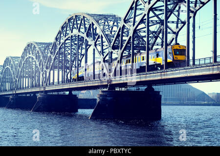 Blau mit gelben elektrischen Zug fährt auf der Eisenbahnbrücke über den Fluss Daugava in Riga Stockfoto