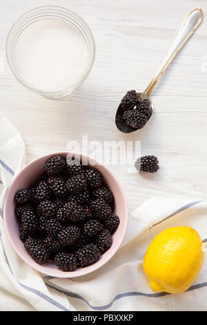 Zutaten für Brombeeren Jam: Beeren, Zitrone, Zucker auf einem weißen Holz- Hintergrund, Ansicht von oben. Von oben und Overhead. Stockfoto