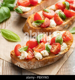 Bruschetta mit Tomaten, Mozzarella und Basilikum auf einem alten rustikalen Tisch. Traditionelle italienische Vorspeise oder Snack, Vorspeise. Stockfoto