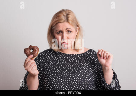 Eine attraktive übergewichtige Frau essen einen Donut, fühlen sich schuldig. Stockfoto