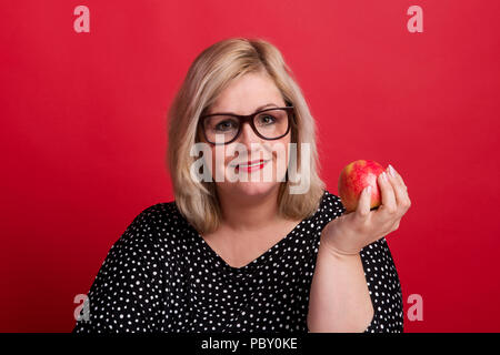 Eine attraktive übergewichtige Frau im Studio, mit einem Apfel in der Hand. Stockfoto