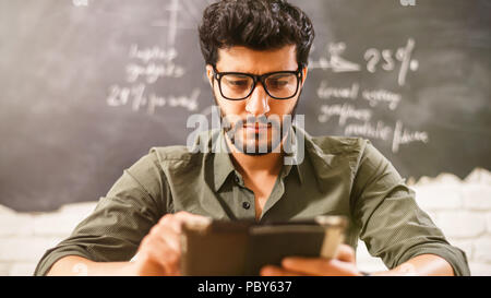 Attraktive multikulturellen bärtigen Geschäftsmann in Gläsern und grünes T-Shirt mit Tablet-PC im Büro auf dem Hintergrund Grafiken Stockfoto