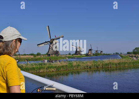 Radfahrerin, die auf der Unesco-Weltanlage Kinderdijk, Südholland, Niederlande, die berühmten Windmühlen neben Kanälen betrachtet Stockfoto