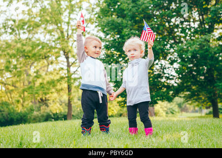 Happy adorable kleine blonde Kaukasische Mädchen und junge, Lächeln, Lachen, Hände und winkte den amerikanischen und kanadischen Flaggen, draußen im Park, Feiern Stockfoto