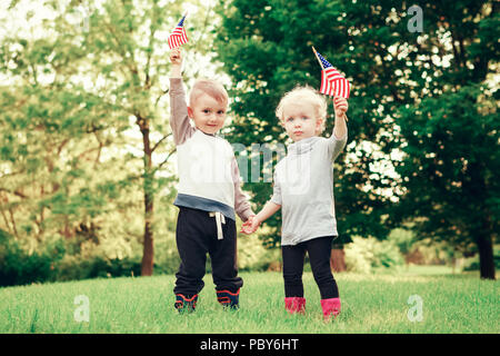 Happy adorable kleine blonde Kaukasische Mädchen und junge, Lächeln, Lachen, Hände halten und wehende Amerikanische Flagge ausserhalb Feiern 4. Juli, Independenc Stockfoto