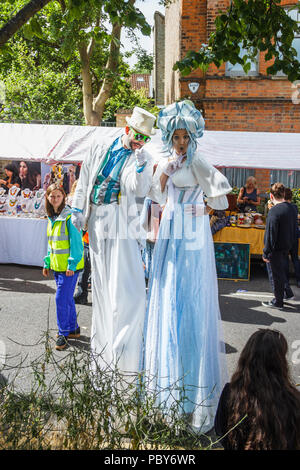 Mann und Frau auf Stelzen in weißen Kostümen an der "fairen gekleidet auf dem Platz", ein jährliches Festival in Highgate, London, UK Stockfoto