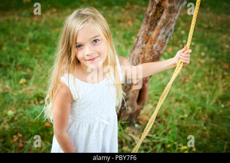 Ein Kind süße Mädchen Schwingen auf einer Strickleiter im Sommer im Garten Stockfoto