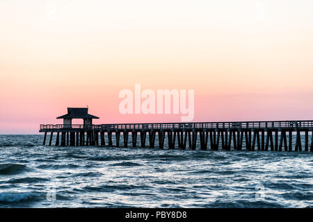 Naples, Florida Pink und Gelb pastell Sonnenuntergang im Golf von Mexiko mit Pier, Holzsteg, mit vielen Säulen über Horizont und Dark Blue Ocean Waves Stockfoto