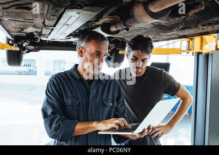 Automechaniker mit Laptop im Auto Reparatur Service mit Kollegen stehen. Auto Service Professionals mit Laptop, während das Auto untersuchen. Stockfoto