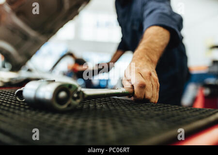 Hand der Mechaniker die Ernte herauf eine Knarre aus der Tabelle im Auto Werkstatt. Mechaniker arbeiten an Garage mit Werkzeug. Stockfoto