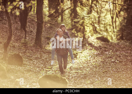 Der Mann mit dem Mädchen gehen bei Sonnenuntergang im Wald, in den Bergen. Mädchen sitzen auf der Kerl zurück. Stockfoto