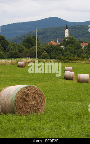 Kroatien, Plitvicer: gelb Heuballen mit grünen Wiesen auf Ackerland in der Landschaft und die Pfarrkirche von der kleinen Ortschaft Drežnik Grad Stockfoto