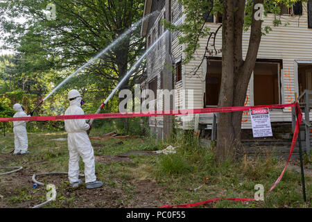 Detroit, Michigan - Verwendung von Schutzkleidung gegen Asbest zu schützen, die Arbeiter bereiten ein verlassenes Haus zu demolieren. Spritzen das Wasser auf