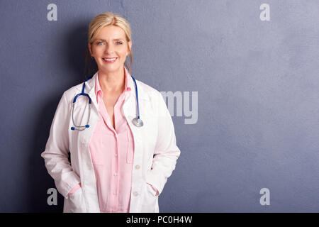 Schuß von lächelnden Frau Doktor mit medizinischen Kleid bei grauen Hintergrund stehend mit kopieren. Stockfoto