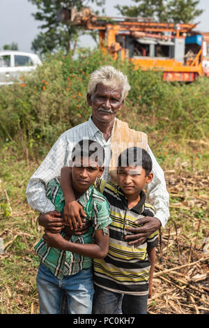 Belathur, Karnataka, Indien - November 1, 2013: Feld Grün- und Brauntönen. Nahaufnahme von Großvater und zwei Enkeln posieren. Wasser bohren Lkw in backgroun Stockfoto