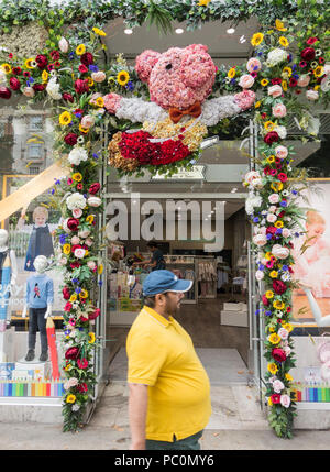 Ein rotun-Mann, der vor einem Blumeneingang um den Kindermode- und Accessoires-Laden Trotters in der Kensington High Street, London, geht Stockfoto