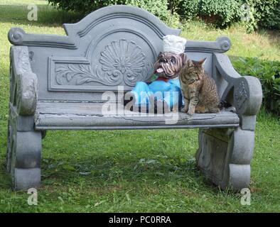 Die hübsche Katze sitzt neben der Abbildung einer Englischen Bulldogge auf der Gartenbank Stockfoto