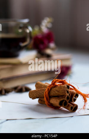 Heiße Tasse Tee über Bücher auf Blau Holztisch, mit Cinnamon Stick mit selektiven Fokus in den Vordergrund und starry Anis mit roten Blumen auf d gebunden Stockfoto