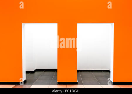 Eine orange Wand mit zwei Öffnungen und weißen leeren Raum dahinter. Stockfoto
