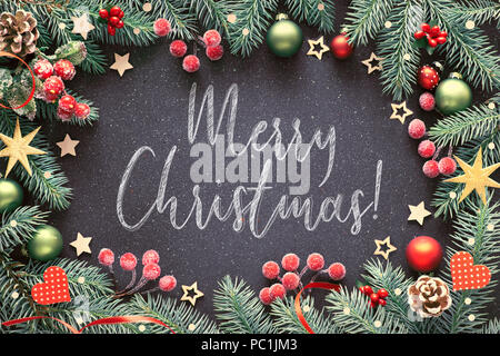 Dekoriert mit dunklem Hintergrund aus Milchglas Beeren und Tannen Zweigen, Text "Frohe Weihnachten!" auf dunklem Hintergrund mit Kreide geschrieben Stockfoto