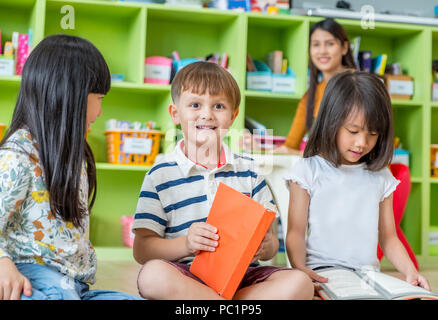 Kinder sitzen auf dem Boden und lesen Märchen Buch im Kindergarten Bibliothek mit Lehrer, Kindergarten Schule Ausbildung Konzept Stockfoto