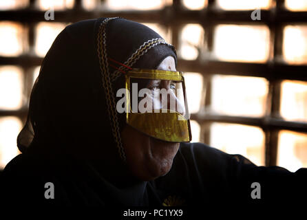 Eine Frau mit einem metallischen Burka strickt Emiratische Flag im Heritage Village in Fujairah. Das Dorf ist zu Reihen, die Emiratische Kultur. Stockfoto