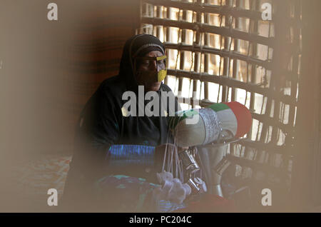 Eine Frau mit einem metallischen Burka strickt Emiratische Flag im Heritage Village in Fujairah. Das Dorf ist zu Reihen, die Emiratische Kultur. Stockfoto