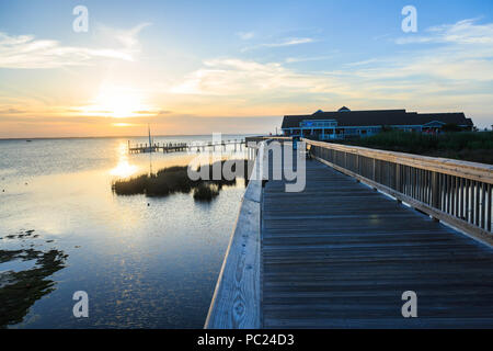 Die untergehende Sonne und Himmel über Currituck Sound Highlight im Vordergrund Boardwalk und entfernten Pier, Seegras, und Waterfront Geschäfte, Ente, NC Stockfoto