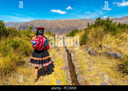 Jungen indigenen Quechua Mädchen in traditioneller Kleidung entlang eine Wasserleitung in der Inca von tipon in der Nähe der Stadt Cusco, Peru ruinieren. Stockfoto