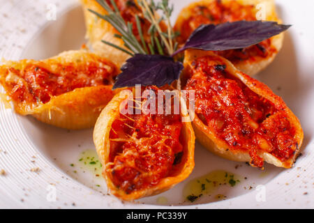 Italienische Pasta Conchiglioni Rigati. Köstliches Gericht gefüllt mit Hackfleisch mit trockenen Tomaten in Tomatensoße. Nahaufnahme auf weißen Teller auf dem Tisch. Stockfoto