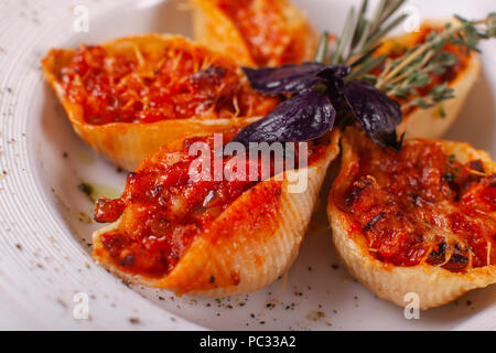 Italienische Pasta Conchiglioni Rigati. Köstliches Gericht gefüllt mit Hackfleisch mit trockenen Tomaten in Tomatensoße. Nahaufnahme auf weißen Teller auf dem Tisch. Stockfoto