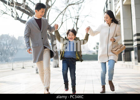 Fröhlicher junger chinesischen Familie halten sich an den Händen zu Fuß Stockfoto