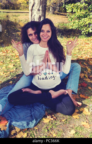 Der Mensch seine schwangere Frau umarmt von der Rückseite auf dem Boden sitzend. Selektiver Fokus Stockfoto