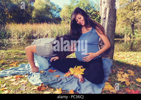 Junger Mann mit langen Locken küssen den Bauch seiner schwanger. Selektiver Fokus Stockfoto