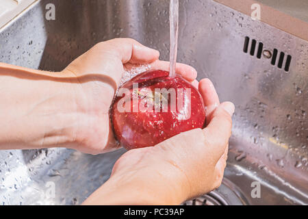 Weibliche Hände waschen red apple im Wasserstrom Küche metallische Kühlkörper Stockfoto