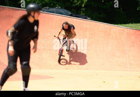 Erwachsene männliche auf BMX Bike Park mit weiblichen Skateboarder im Vordergrund Stockfoto