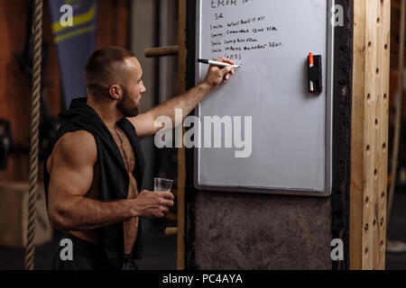 Angenehme muskulösen Mann schreiben Workout Routine auf das Flipchart mit einem Rest. nach oben Seitenansicht Nahaufnahmen Stockfoto