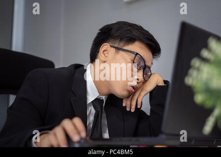 Junge Geschäftsmann schläfrig auf Schreibtisch zwischen mit Laptop Stockfoto