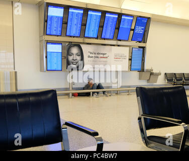 Teenager auf seinem Mobiltelefon am Boden unterhalb der An- und Abreise Bildschirme bei George Bush International Airport in Houston, Texas, USA sitzen. Stockfoto