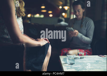 Zwei junge Frauen sind Trinkwasser und über Telefone in einem Cafe Stockfoto