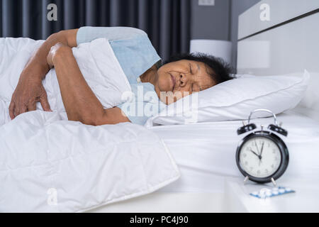 Ältere Frau schlafen in einem Bett mit einer Uhr Stockfoto