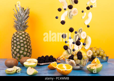 Zusammensetzung des Fliegens Früchte und tragende in einer Schüssel mit köstlichen Dessert Salat auf einem gelben Hintergrund Stockfoto