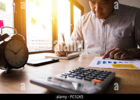 Buchhalter berechnen Finanzierung der jährlichen Profit durch Drücken der Rechner und fasste balance Geld durch Schreiben auf Hinweis buchen Sie im Büro Stockfoto