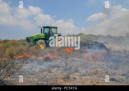 Landwirt pflügt ein brennendes Feld, um das Feuer zu enthalten. Dieses Feuer war verursacht durch palästinensische Kite Bomben, die aus dem Gazastreifen geflogen wurden mit einer beleuchteten Benzin getränkt Stockfoto