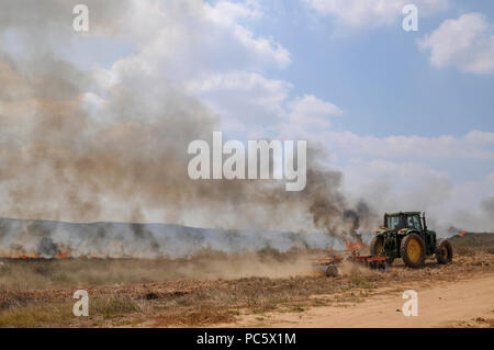 Landwirt pflügt ein brennendes Feld, um das Feuer zu enthalten. Dieses Feuer war verursacht durch palästinensische Kite Bomben, die aus dem Gazastreifen geflogen wurden mit einer beleuchteten Benzin getränkt Stockfoto