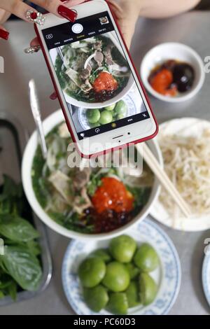 Schüssel vietnamesische Nudelsuppe Pho genannt. Frau, die Bild mit Smartphone Ihrer Mahlzeit. Ho Chi Minh City. Vietnam. | Verwendung weltweit Stockfoto