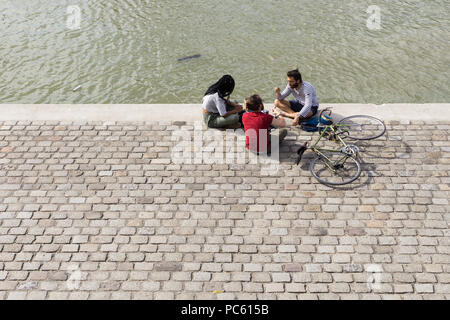 Freunde in der Nähe von Wasser - drei Freunde von oben sitzen und plaudern auf einem Kanal Bank gesehen. Stockfoto