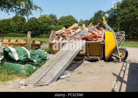 Behälter mit Schutt und Schubkarre im Außenbereich Stockfoto